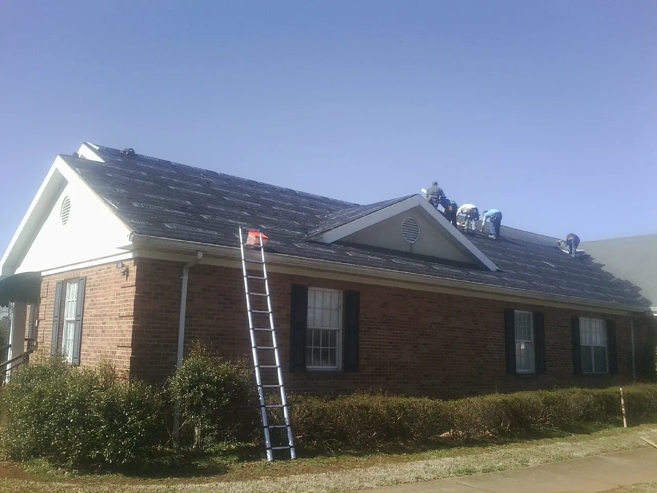 Crew tearing shingles off a brick ranch roof with a ladder set — Emergency Roof Repair work by our crew in Pennsburg