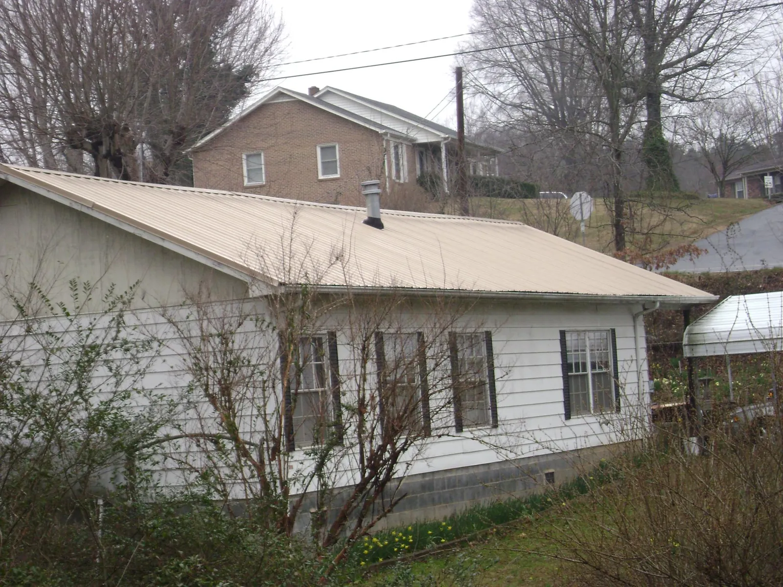Tan metal roof on a white sided house set into a hillside — Commercial Roofing by Roofing Brothers in Pennsburg